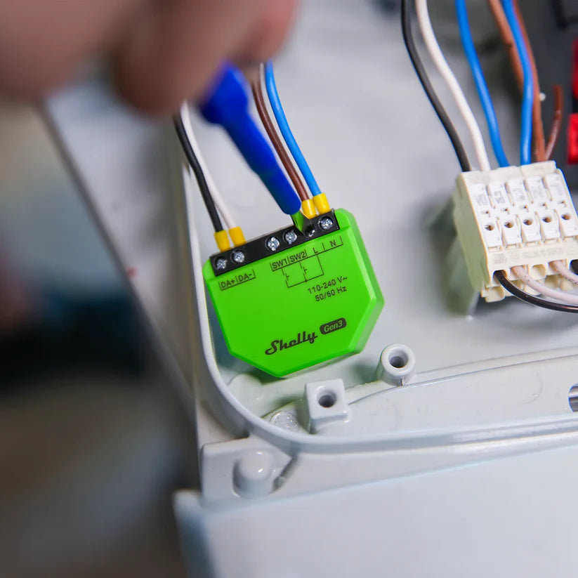 Green electronic device with wires being connected, brand 'Shelly' visible
