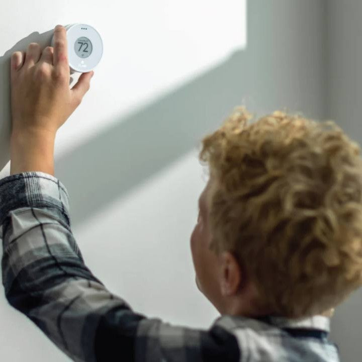 Child adjusting a thermostat on a wall