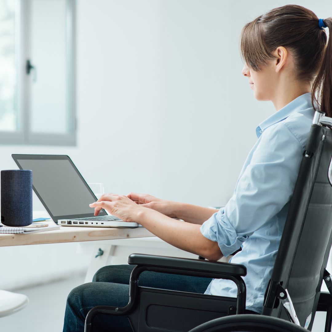Woman in a wheelchair working with a computer and a voice control system on the desk