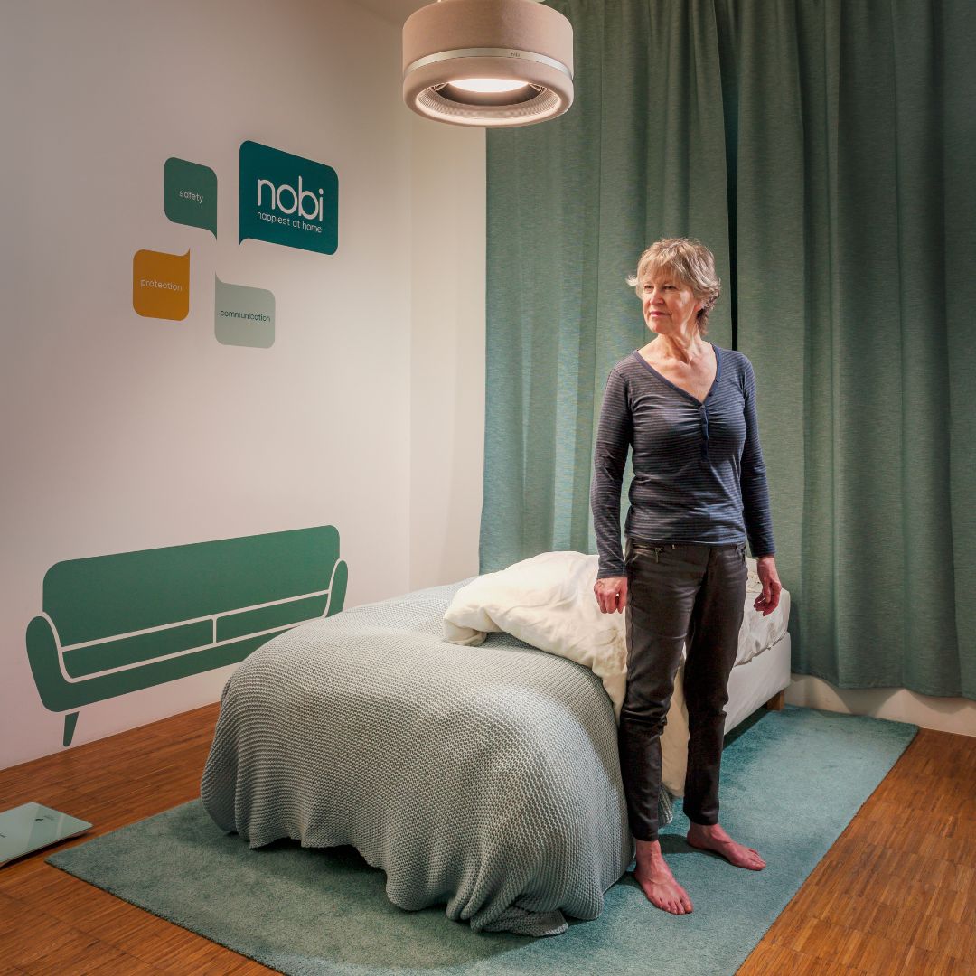 an older adult standing next to the bed, with the dim light of nobi