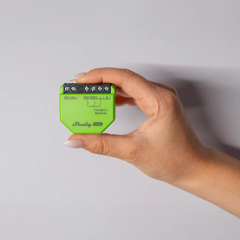 Hand holding a green electronic device with 'Shelly' branding against a light gray background