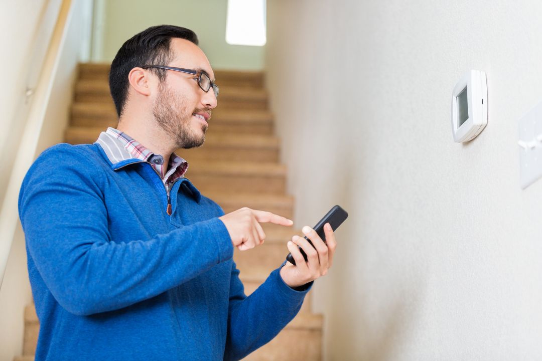 man with phone looking at thermostat